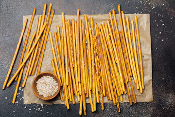 Salted bread sticks or long crunchy salty pretzel sticks on parchment paper on old brown stone or...
