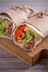 Homemade tasty burrito with tuna fish, cucumber, avocado and carrot. Tuna wraps on wooden background. vertical