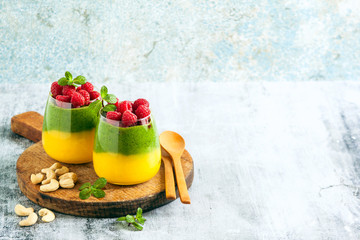 Fresh vegan layered dessert in a glass of colored smoothies of mango and spinach with fresh raspberries and mint.