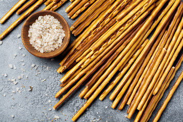 Salted bread sticks or long crunchy salty pretzel sticks on parchment paper on old gray stone or...