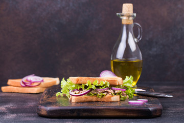 Tuna fish sandwich with onion, lettuce and olive oil on a wooden board.