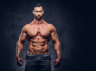 Fototapeta na wymiar Portrait of a shirtless tall huge male with a muscular body with a stylish haircut and beard, in a sports shorts, standing in a studio.