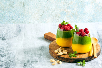 Fresh vegan layered dessert in a glass of colored smoothies of mango and spinach with fresh raspberries and mint.