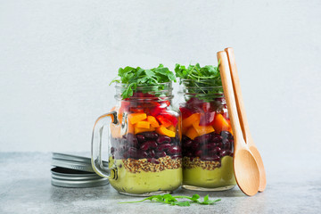 rainbow colored salad in jars on the table. with beans, fresh vegetables and avocado dressing with lime juice and mustard. copy space.