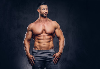 Fototapeta na wymiar Portrait of a shirtless tall huge male with a muscular body with a stylish haircut and beard, in a sports shorts, standing in a studio.
