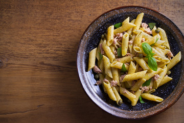 Tuna, basil and caper penne with pesto sauce in bowl on wooden background. Pasta with tuna fish. overhead, horizontal