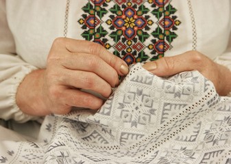 Woman in ukrainian national shirt embroiders on white linen