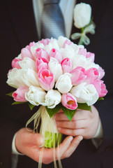 Big bridal bouquet of white and pink fresh tulips in hands of groom in black suit. Vertical color photography.