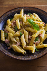 Tuna, basil and caper penne with pesto sauce in bowl on wooden background. Pasta with tuna fish. overhead, horizontal