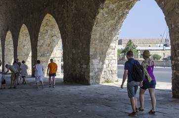 Fototapeta na wymiar Heraklion, Crete Island / Greece. View of the old Venetian Shipyards near the old port of Heraklion city. Through the first arch we see part of the fortress Koules. Tourists enjoying their walk 