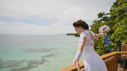 Fototapeta na wymiar A dazzling bride enjoys happiness from the height of the balcony overlooking the ocean and reefs. Flight of love. Exotic Filipino Tropics. Shooting in motion.