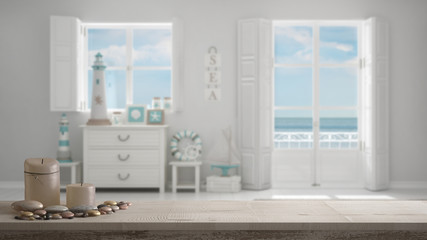 Wooden vintage table top or shelf with candles and pebbles, zen mood, over blurred mediterranean white living, windows with sea panorama, white architecture interior design