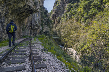 Hiking at Vouraikos gorge following the Diakopto–Kalavrita "Odontotos" rack railway route. Peloponnese - Greece. Caucasian man with a backpack is following the railroad enjoying the beautiful nature