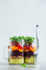rainbow colored salad in jars on the table. with beans, fresh vegetables and avocado dressing with lime juice and mustard. copy space.