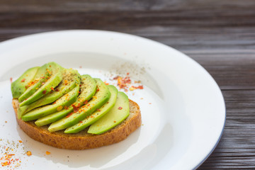 Toast with cutted avocado and spices in white plate on brown wooden background. Close-up