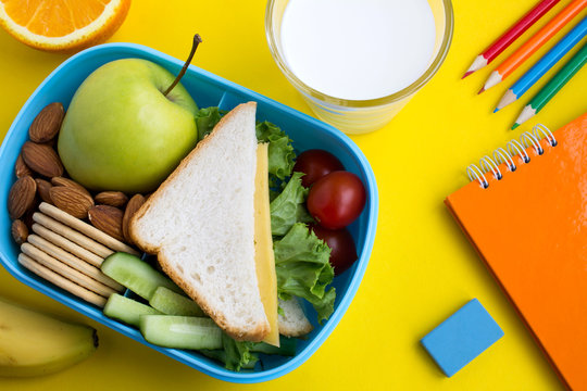 School lunch in the box, milk in the glass and notebook on the yellow background.Top view.