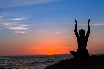 Silhouette of yoga woman meditation on the ocean during amazing sunset.