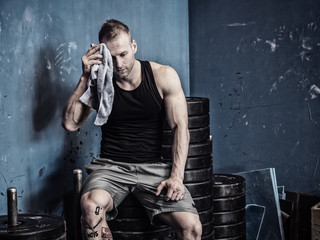 Muscular young bodybuilder drying sweat from his face with a towel after workout in a gym. Tattoo reads: Life is a carnival. And: Noise.