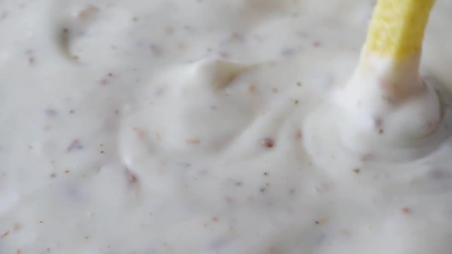 Slow motion close video of stirring ranch dressing with a yellow veggie straw.