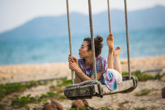 A young mixed race woman swinging on a wooden swing at a seaside tropical beach.