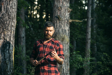 Naklejka na ściany i meble Brutal lumberjack looking at small sharp spade in his hands. Lone hiker in woods. Summer night camping