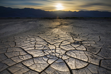 Big mud cracks light up in golden hour light with a sunset over the distant mountains - 202232202