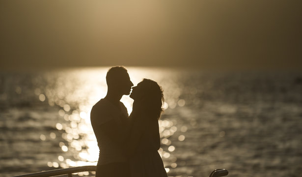 Silhouette of sensual couple kissing with sunset above sea surface on background. Couple in love on romantic date in evening at seafront, defocused, copy space. Romance and love concept.