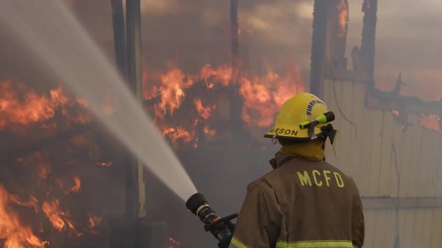 Fireman spraying water on the fiercely burning interior of a structure almost demolished by flames