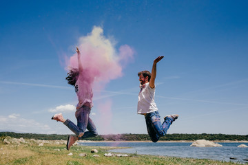 Lovely couple having fun outdoors playing with colorful holi powder jumping and laughing. Lifestyle portrait