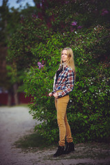 Fototapeta premium pretty woman blonde on a rustic road is happy, against a background of lots of green trees, a beautiful portrait of a rustic style, a simple home image