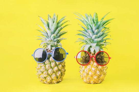 Pineapples with red and blue sunglasses on yellow background - Summer background