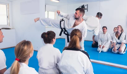 Abwaschbare Fototapete Kampfkunst Der bärtige, lächelnde Trainer zeigt Erwachsenen neue Kampftechniken