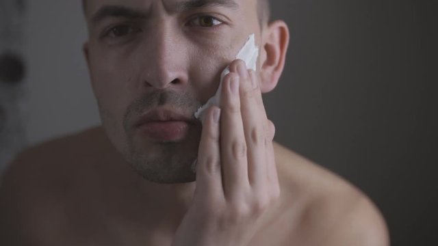 Man shaving with foam and manual razer. Close up of man shaving beard.