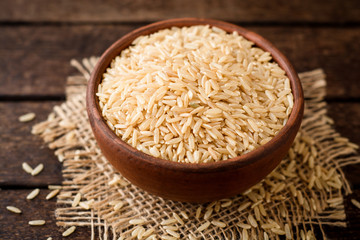 Raw brown rice in ceramic bowl on dark rustic wooden background