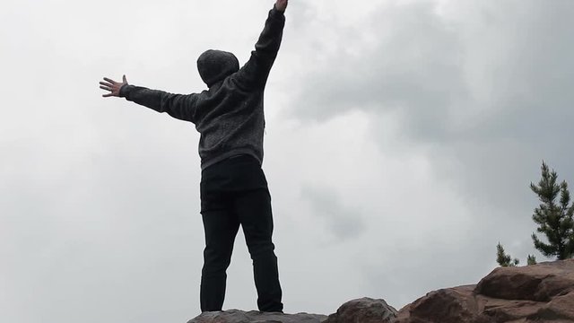 A man standing on top of a mountain and spreading his arms against the background of clouds and sky