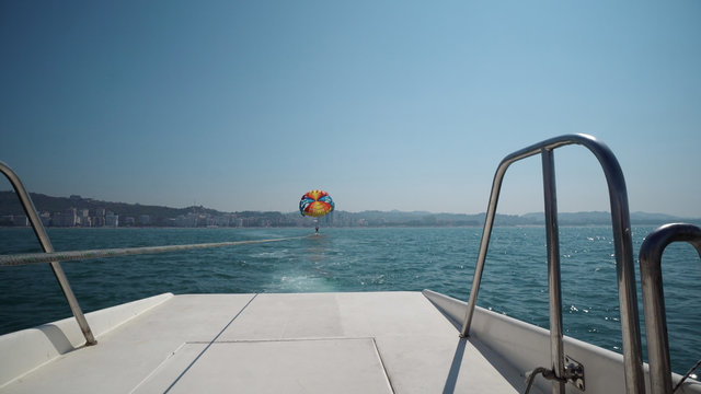 Excited tourists parasailing high in the sky, extreme sport, summer activities, POV from behind the yacht boat