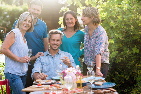 Group of friends gathered around a table in a garden on a summer evening to share a meal. They are posing for a photo