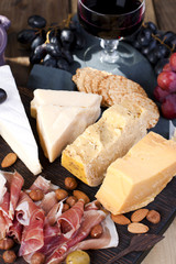 A glass of red wine and a snack. Grapes, cheese, biscuits, olives, ham. Italian food. Vertical photo