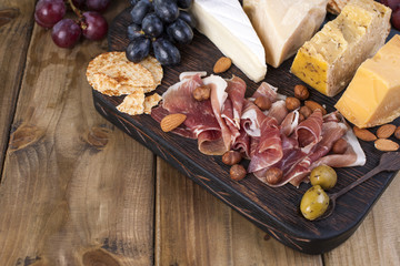 Different snacks. Grapes, cheese, crackers, olives, ham. Italian food.