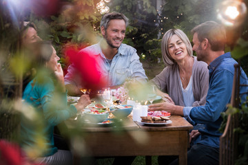 A summer evening of friends in their 40s gather around a table in the garden to share a meal and have fun together.