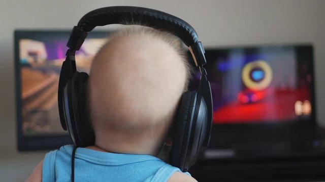 Baby boy in headphones playing the computer game. The concept of computer addiction, selective focus.