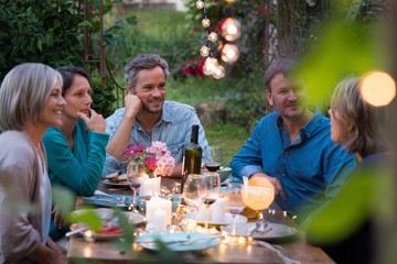 Group of friends gathered around a table in a garden on a summer evening to share a meal and have a good time together