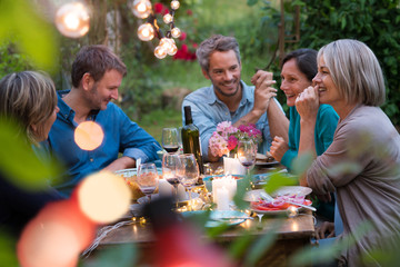 Beautiful summer evening in the garden, a group of friends in their forties have a good time laughing together around a table.