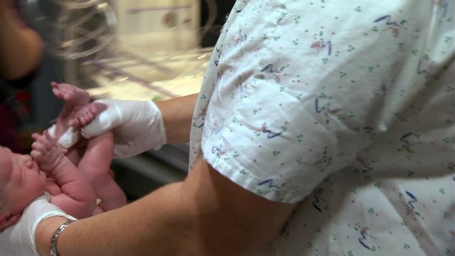 Nurse lifting newborn baby boy onto scales