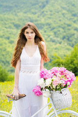 Fototapeta na wymiar Gorgeous young bride in white crochet vintage dress outdoors in spring with bike and basket full of flowers