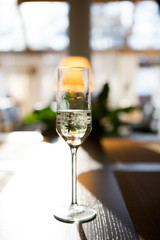 A glass of champagne shitoit on a dark wooden table in the setting sun