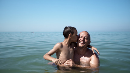 Fototapeta premium Father and son playing at beach together portrait fun happy lifestyle, boy embrace father kiss him
