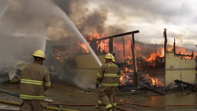 Firemen walking over to stand by a co-worker spraying flames in a burned house