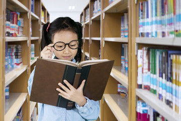 Little girl reading a textbook in the library