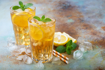 Traditional iced tea with lemon, mint and ice in tall glasses. Two glasses with cool summer drink on old rusty background